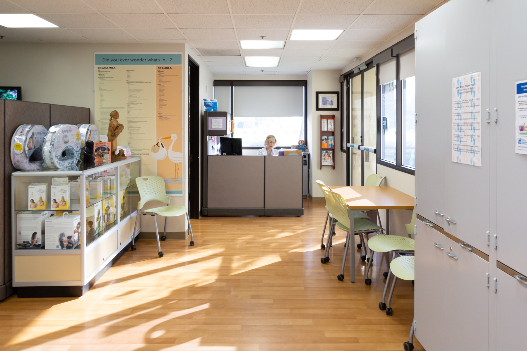 Interior del Centro de recursos para madres que muestra un mostrador de recepción, carteles informativos en la pared y productos para la lactancia materna en una vitrina.