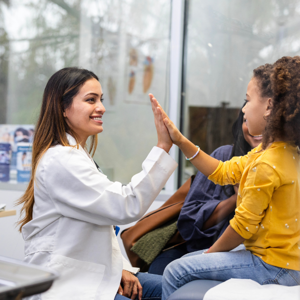 Una doctora latina joven choca los cinco con su paciente, una preadolescente negra con camiseta amarilla.